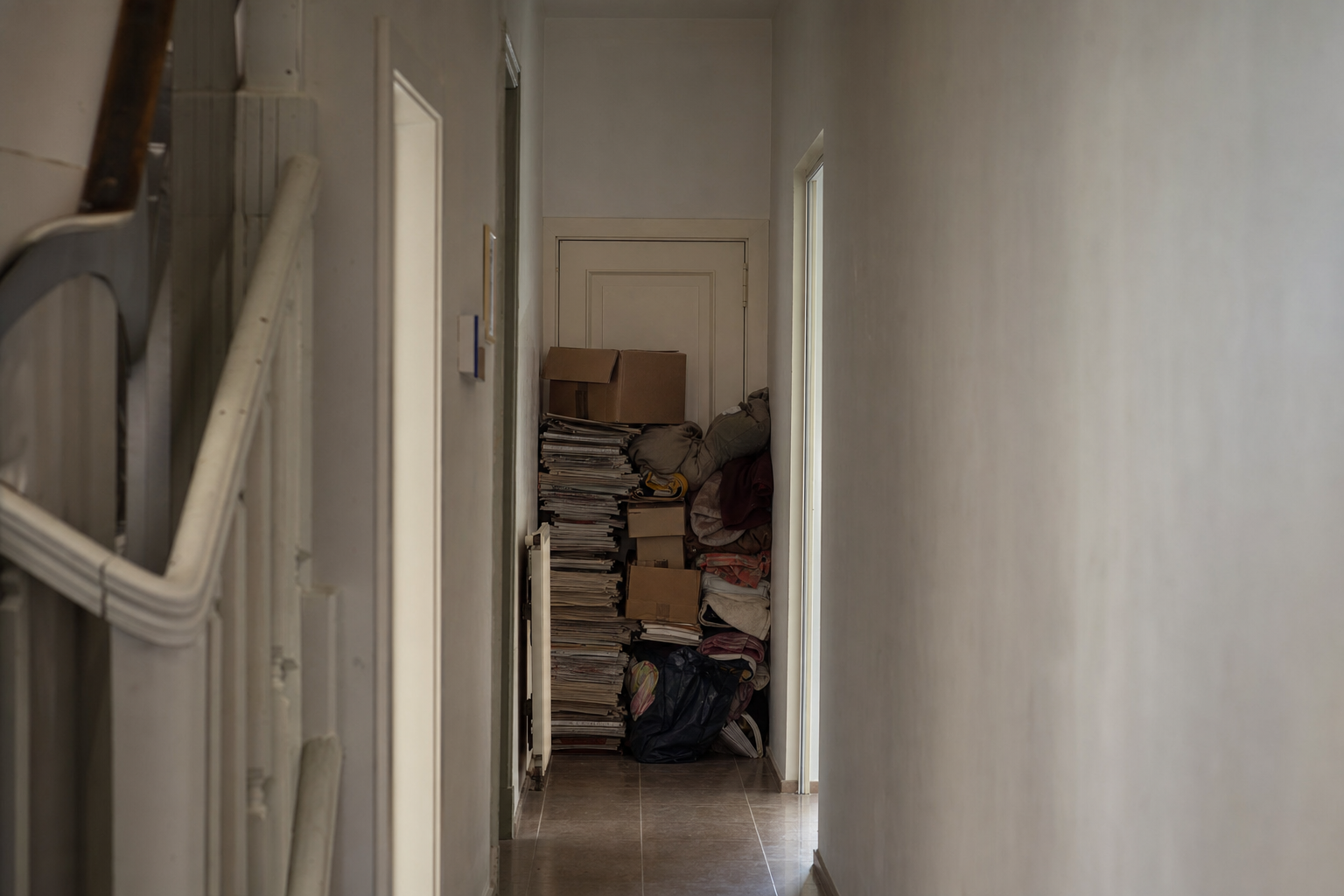 Geblokkeerde deur met opgestapelde kranten, dozen en textiel ervoor in een woning